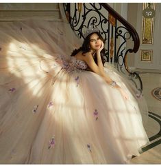 a woman in a ball gown sitting on the stairs with her hand under her chin