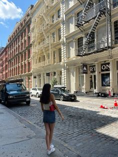 a woman is walking down the street in front of some buildings with cars parked on it