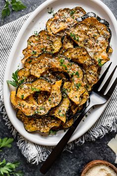 cooked eggplant with parsley on a white plate next to a knife and fork