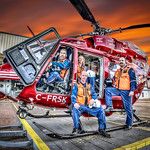 two men standing in front of a red helicopter with the door open and people inside