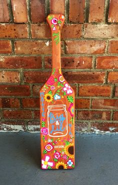 a painted wooden bottle sitting in front of a brick wall