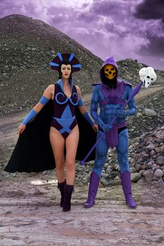 two people dressed in costumes are walking on a rocky area with a skull and pumpkin