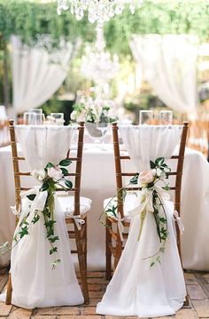 two wooden chairs decorated with white flowers and greenery sit in front of a table