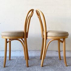 two wooden chairs sitting next to each other on top of a carpeted floor in front of a white wall