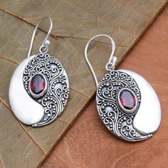 An oval pool of natural garnet is reflected in a larger oval of sterling silver. Eka Devi crafts these beautiful dangle earrings elaborating them wit traditional Balinese motifs.