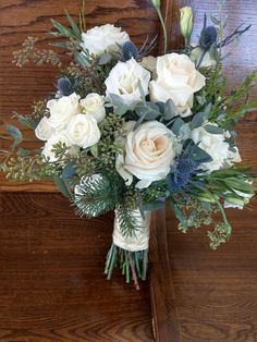 a bouquet of white roses and greenery on a wooden table in front of a wall