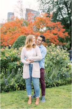 an engaged couple standing together in front of colorful trees and bushes during their engagement session