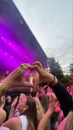 two people making a heart shape with their hands in front of a crowd at a concert