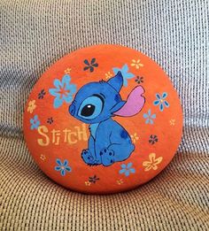 an orange button with stitch on it sitting on top of a gray couch next to a blue flowered pillow