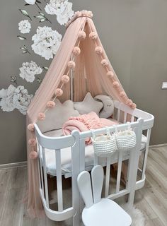 a white crib with pink and white flowers on the wall next to a chair