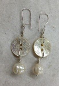 two white seashells are hanging from silver earwires on a marble surface