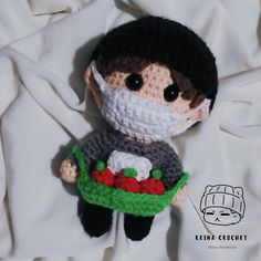 a crocheted doll wearing a face mask and holding a green basket with red flowers