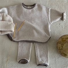 an infant's sweater and hat are laid out on the floor next to a rock