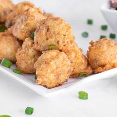 some fried food is on a white plate and green onions are in the bowl next to it