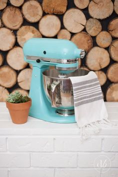 a blue mixer sitting on top of a counter next to a pile of logs and a potted plant