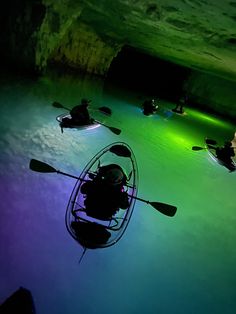 several people in kayaks are floating on the water at night with green and purple lights