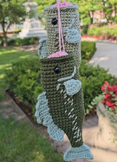 a crocheted fish ornament hanging from a string in front of some bushes