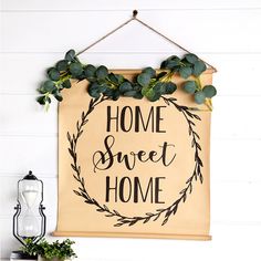 a sign hanging on the wall that says home sweet home with greenery around it