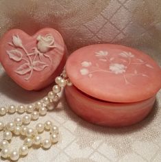 a pink heart shaped box next to a pearl necklace