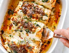 someone holding a spatula over some food in a casserole dish with cheese and spinach