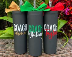 three black tumblers with bows on them are sitting on a table in front of some flowers