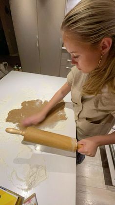 a woman rolling out dough on a counter top with a wooden rolling pin in front of her