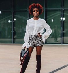 a woman with red hair is standing in front of a building wearing boots and a white blouse