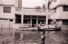 a man standing in the water next to a car and a boat with people on it