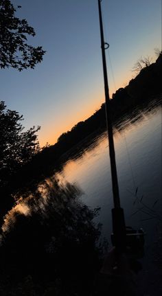 a fishing pole is next to a body of water with trees in the background at sunset