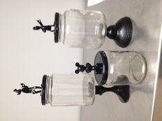 three glass jars with figurines on top of them sitting on a metal surface