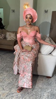 a woman wearing a pink dress and head wrap sitting on a couch in a living room