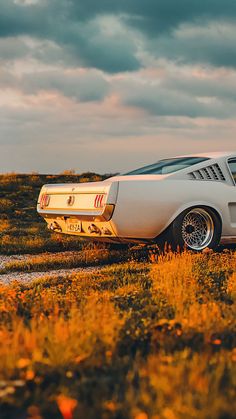 an old car parked on the side of a road in a grassy field under a cloudy sky