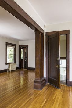 an empty living room with wood floors and wooden pillars in the center, looking into another room