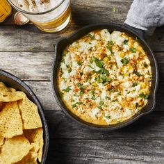 a pan filled with cheese and chips next to a glass of beer on top of a wooden table