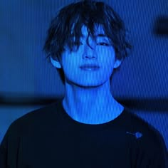 a young man in a black shirt is staring at the camera with blue light behind him