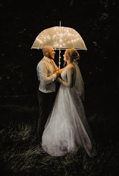 a bride and groom standing under an umbrella in the dark with fairy lights on it