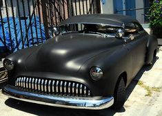 an old black car parked in front of a fence