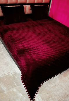 a bed with a red bedspread on top of it next to a pink headboard