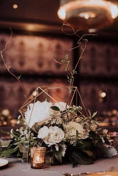 a centerpiece with white flowers and greenery on a table