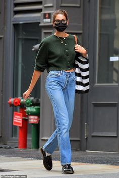 a woman walking down the street wearing a face mask and carrying a black handbag