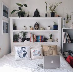 a bed with a laptop on top of it next to bookshelves and plants