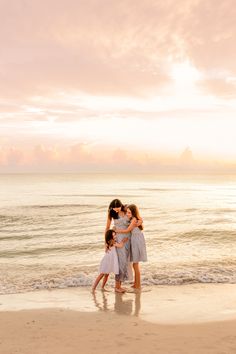 three women standing on the beach with their arms around each other as they hug and kiss