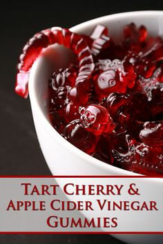 a white bowl filled with red candies on top of a black table next to the words tart cherry and apple cider vinegar gummies