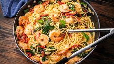 pasta with shrimp, spinach and sun dried tomatoes in a pan on a wooden table