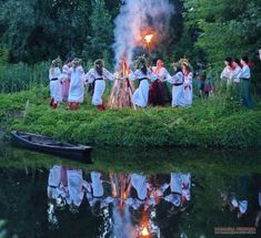 a group of people standing next to a lake with a fire in the middle of it