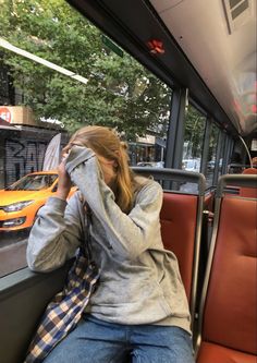 a woman sitting on a bus with her head in her hands while talking on the phone