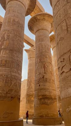 two people standing in front of some very large pillars with carvings on them and one person looking up at the ceiling