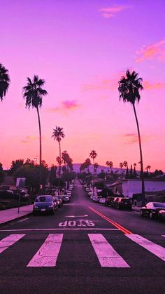 palm trees line the street as the sun goes down in this pink and purple sunset