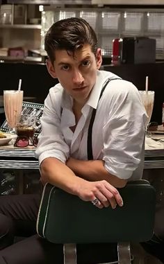 a man sitting in a chair with his arms crossed and looking at the camera while he is wearing suspenders