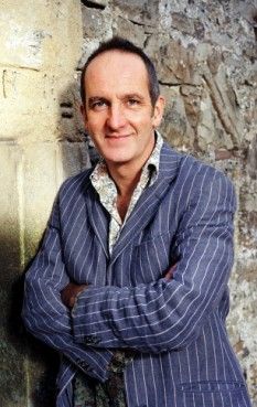 a man standing in front of a stone wall with his arms crossed and looking at the camera